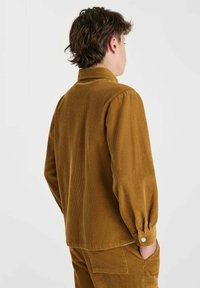 Bruine corduroy overhemd met een kraag, lange mouwen en knoopmanchetten. Heeft verticale strepen en een losse pasvorm. Achteraanzicht weergegeven.
