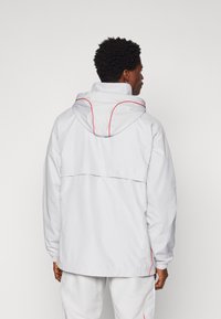 Witte capuchonjack met rode accenten, met een relaxte pasvorm, elastische manchetten en een ventilatieluik aan de achterkant voor ademend vermogen.