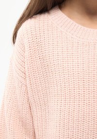 Jasnoróżowy sweter dzianinowy z okrągłym dekoltem i luźnymi rękawami. Tekstura jest miękka i ma nieco grubszy splot.