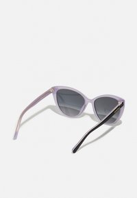 Cat-eye sunglasses with a translucent lavender frame, dark gray lenses, and black arms featuring a gold accent.