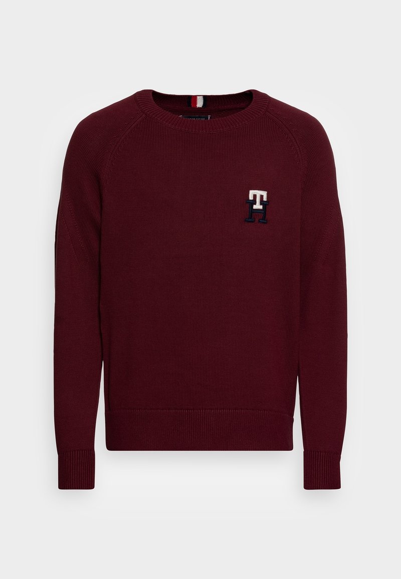 Pull à col rond couleur marron avec poignets et ourlet côtelés, présentant un petit logo brodé "TH" sur le côté gauche de la poitrine.