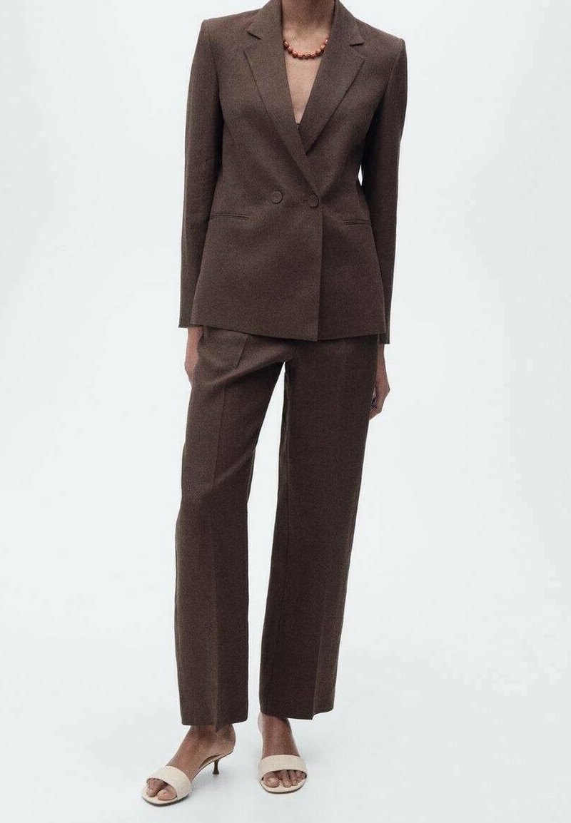 Hnědý přizpůsobený blazer se dvěma knoflíky a špičatými klopami, v kombinaci s odpovídajícími kalhotami s rovnými nohavicemi. Nosené s béžovými otevřenými sandály na podpatku.