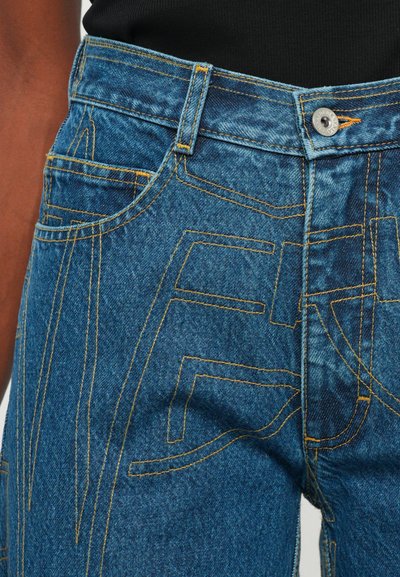 Modré džíny z denimu s kontrastním žlutým prošíváním, vysokým pasem a jedinečným texturovaným vzorem na přední straně, včetně velkých písmen.