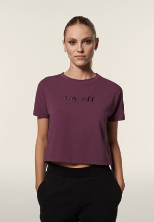 T-shirt cropped viola realizzata in morbido cotone con scollatura rotonda. Presenta testo in rilievo "giorno di riposo" sul davanti e maniche corte.
