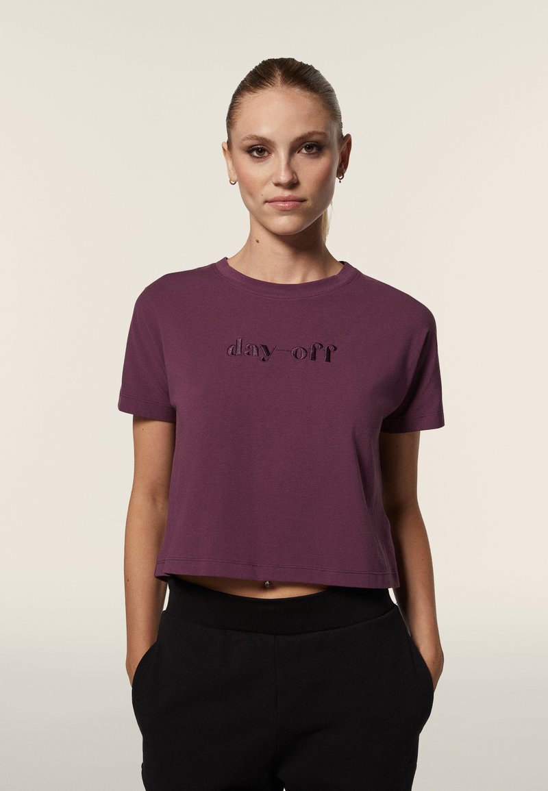 Camiseta corta morada de algodón suave con escote redondo. Presenta un texto en relieve "día libre" en el frente y mangas cortas.