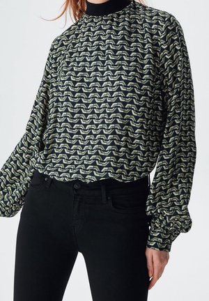 Blouse à manches longues avec un col haut, motif vagues noir et crème, coupe loose et poignets élastiqués, associée à un jean skinny noir.