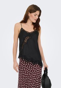 Camisole en soie noire avec bordure en dentelle et bords festonnés, dotée de fines bretelles et d'un design superposé, associée à une jupe bordeaux à pois.