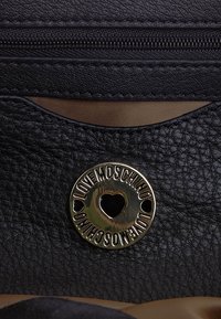 Black textured leather handbag featuring a gold-tone round logo with a heart cutout, a zip closure, and a smooth interior lining.