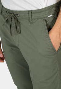 Pantalones cortos de cargo verde oliva con cinturilla elástica, cierre de cordón, bolsillos frontales y tejido suave y ligero.
