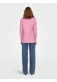 Blazer fucsia su misura con maniche a tre quarti, caratterizzato da una linea dritta. Abbinato a jeans blu larghi, visto da dietro.