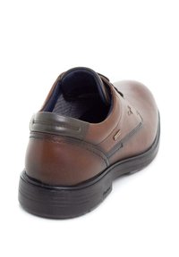 Zapato de cuero marrón con forma redondeada, parte superior texturizada, acentos oscuros y una suela de goma negra. Presenta un pequeño logo de la marca.