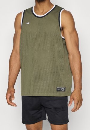 Mężczyzna w oliwkowo-zielonym sportowym bezrękawniku i czarnych spodenkach, stojący z ramionami swobodnie opuszczonymi wzdłuż ciała na jednolitym tle.