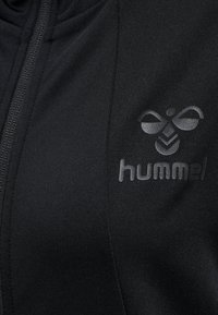 Czarna sportowa kurtka wykonana z fakturowanej tkaniny, z zamkiem błyskawicznym i tonalnym logo na lewej piersi.