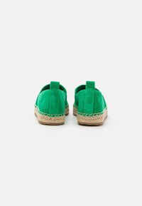 Espadrilles vertes en suède avec semelles en jute tressé, vues de dos sur un fond blanc uni.