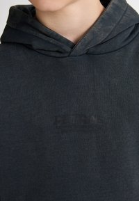 Donkergrijze katoenen hoodie met een trekkoord, voorzien van een subtiele logoafdruk in het zwart op de borst. Soepele textuur en eenvoudig ontwerp.
