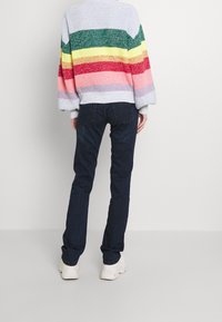 Striped knit sweater in blue, yellow, red, and pink; paired with dark blue jeans and white footwear. Soft texture and oversized fit.