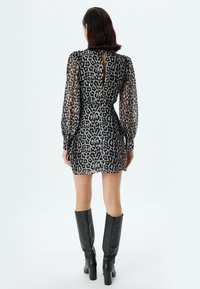Leopardprint jurk met doorschijnende zwarte lange mouwen, open rug en een getailleerde taille. Gepaard met zwarte leren laarzen tot de knie.