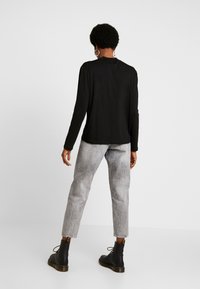 Musta pitkähihaine paita yhdistettynä vaaleanharmaisiin, hieman kuluneisiin, kapeisiin farkkuihin ja mustiin nilkkabootseihin, joissa on koristeellista metallia.