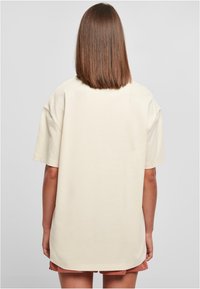Krämfärgad oversized T-shirt med korta ärmar, tillverkad av mjuk bomull. Har en enkel, ren design, rak fåll och inga synliga logotyper.