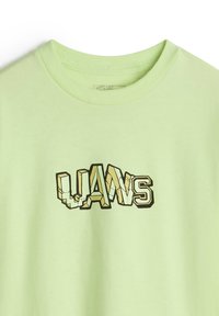 Ljusgrön bomullst-shirt med en stiliserad grafisk design där ordet "LWANS" framträder i en blandning av fetstil och konturerade bokstäver.