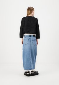 Veste noire cropped avec une texture en tissage ouvert, associée à une longue jupe en denim bleu. Des chaussures à plateforme noires complètent la tenue.