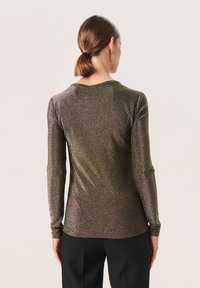 Maglione a maniche lunghe in tessuto metallico scuro con una superficie scintillante. Presenta un collo rotondo e una silhouette aderente. Pantaloni neri visibili.