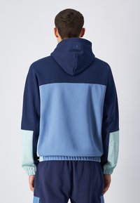 Felpa con cappuccio caratterizzata da blocchi di colore blu, vestibilità rilassata, polsini elasticizzati e un pannello posteriore testurizzato. Realizzata in morbido cotone.