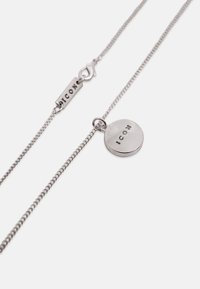 Collier chaîne en argent avec un pendentif rond et une étiquette à fermoir, tous deux gravés du mot « ICON » en lettres majuscules.