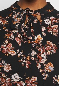 Czarna sukienka w kwiaty z różowymi, pomarańczowymi i białymi wzorami. Posiada wiązany dekolt oraz miękką, zwiewną fakturę materiału.