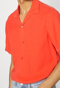 Korte mouw blouse in fel koraal, gemaakt van lichtgewicht stof. Voorzien van een knoopsluiting aan de voorkant en een comfortabele pasvorm met kraag.