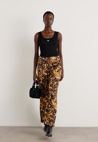 Top senza maniche nero, pantaloni a vita alta con stampa leopardata in beige e nero, tessuto texture, abbinati a una piccola borsa nera e stivaletti.