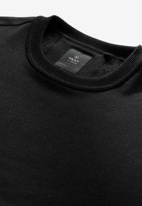Sort bomulds sweatshirt med ribbet halsudskæring, med et mærke på bagsiden med brandnavnet "NEXT" og plejeinstruktioner.