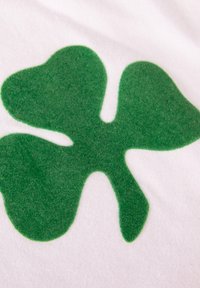 Witte stof met een groot groen klavertje vier ontwerp, met een textuur die licht verhoogd is tegen de gladde achtergrond.