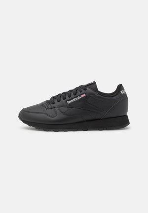 Baskets de sport noires à tige en cuir, fermeture à lacets, détails texturés, semelle rembourrée et logo Reebok sur le côté.