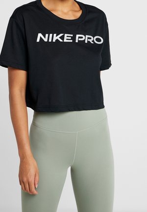 Osoba ubrana w czarny krótki t-shirt Nike Pro oraz jasnzielone, dopasowane legginsy z wysokim stanem na jednolitym tle.