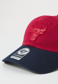 Șapcă roșie cu un logo brodat al echipei Chicago Bulls pe față, cu bor rămăsese albastru închis și curea ajustabilă. Conține eticheta de marcă.