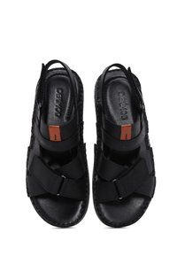 Sandalias negras con un acabado de cuero suave, que cuentan con correas ajustables, una suela plana y un pequeño acento naranja cerca del talón.