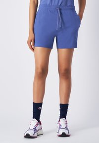 Niebieskie bawełniane szorty z elastycznym paskiem w talii i sznurkiem, z bocznymi kieszeniami. W zestawie z granatowymi skarpetami w prążki i białymi trampkami.