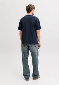 Μπλε ναυτικό βαμβακερό μπλουζάκι με άνετη εφαρμογή, κοντά μανίκια και στρογγυλή λαιμόκοψη, συνδυασμένο με ανοιχτόχρωμα μπλε τζιν και μπεζ παπούτσια.