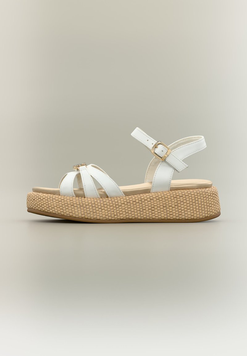 Λευκό σανδάλι με λουράκια και ρυθμιζόμενο αγκράφα στον αστράγαλο, με μπεζ υφαντή σόλα πλατφόρμας, εμφανιζόμενο σε πλαϊνή όψη σε ουδέτερο φόντο.