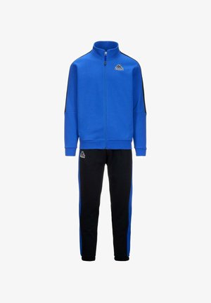 Sudadera azul con cremallera y detalles en negro, combinada con pantalones deportivos negros que tienen franjas laterales azules. Hecha de un tejido suave y texturizado.