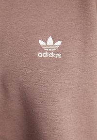 Sweatshirt Adidas em tecido mauve suave com um acabamento texturizado. Apresenta um logótipo bordado com um design de três folhas em branco.