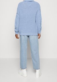 Maglione lavorato a maglia blu chiaro con motivo a trecce, vestibilità oversize, spalle scese, abbinato a jeans in denim chiaro e scarpe con piattaforma bianche.