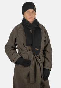 Black knitted beanie, scarf, and gloves with a textured finish, paired with a grey wool coat featuring a belt and buttoned cuffs.