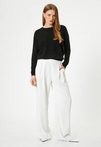 Maglione nero lavorato a maglia con maniche lunghe abbinato a pantaloni bianchi a gamba larga. I pantaloni presentano una superficie liscia e tasche laterali nascoste.