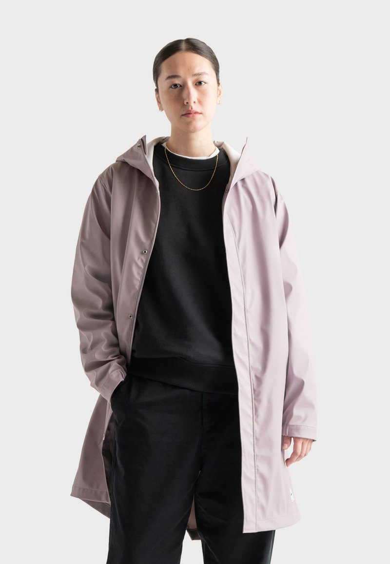 Svetlofialová vodeodolná bunda s kapucňou, cvočkami a bočnými vreckami, prekrývajúca čiernu mikinu a čierne nohavice.