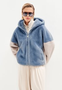 Giacca con cappuccio e zip in blu chiaro e beige, realizzata in morbido materiale soffice. Presenta una vestibilità rilassata e un design a blocchi di colore a contrasto.