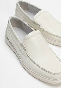 Zapatos slip-on de cuero gris claro con superficie texturada, costuras sutiles y paneles elásticos laterales. Suela de goma suave para mayor comodidad.