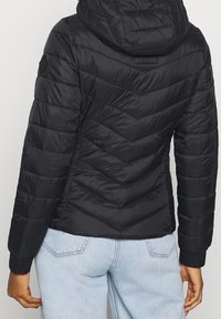 Doudoune noire avec capuche, arborant un design matelassé en chevrons et des poignets côtelés. Le tissu a une texture lisse et brillante.