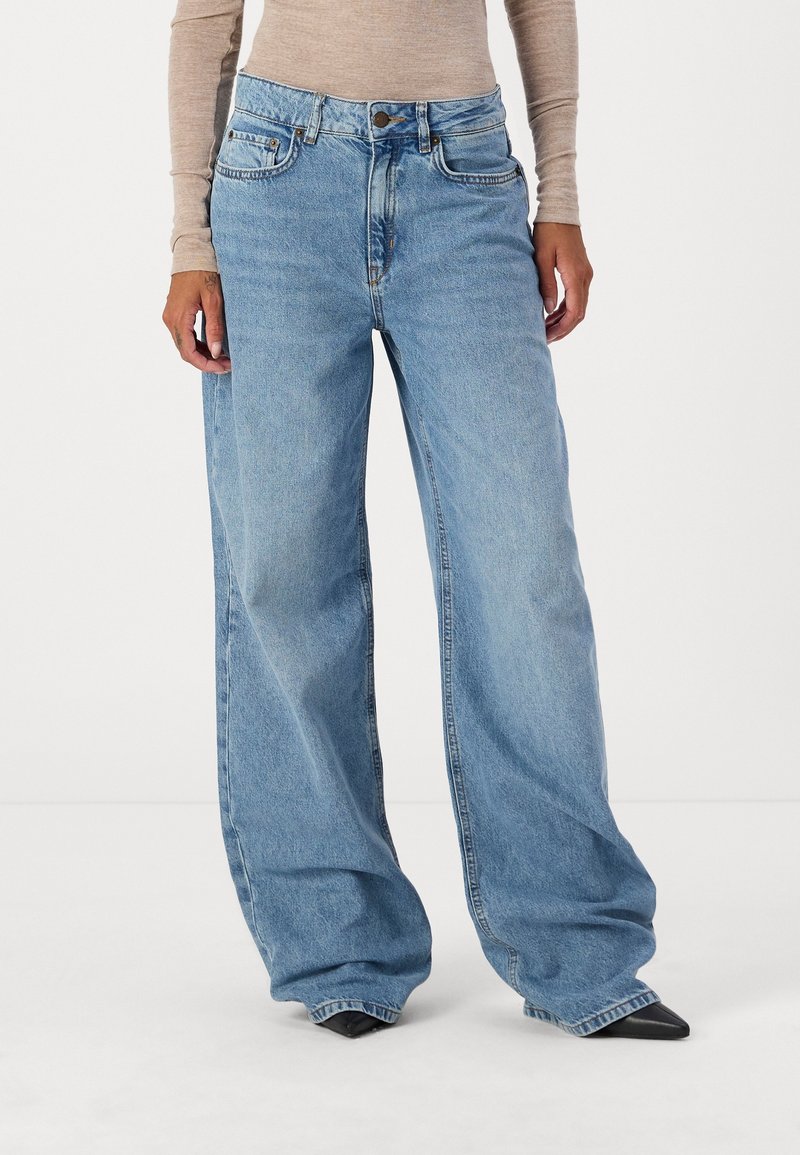 Vaqueros de mezclilla de pierna ancha en azul claro, con una cintura alta, cinco bolsillos y detalles de costura visibles.